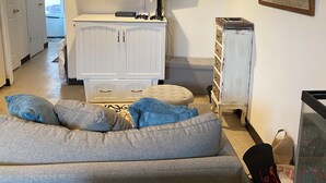 A compact living space with a sofa, a mounted TV, a framed artwork, and a small table. - Cheeseburgers in Paradise (Long Beach)