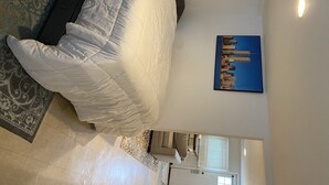 A room with a bed, a patterned rug, a cityscape painting, and a door. - Cheeseburgers in Paradise (Long Beach)
