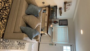 A living room with a beige sofa, two blue pillows, a patterned rug, and a white door with a window. - Cheeseburgers in Paradise (Long Beach)