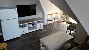 A compact, modern loft bedroom with a sloped ceiling, a built-in TV, a wooden dining table, and two chairs. - Beautiful, Cozy Condo with large private deck! (Cape May)