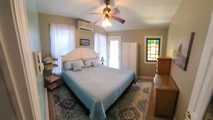 A bedroom with a bed, a ceiling fan, a window with stained glass, and a door. - Beautiful, Cozy Condo with large private deck! (Cape May)