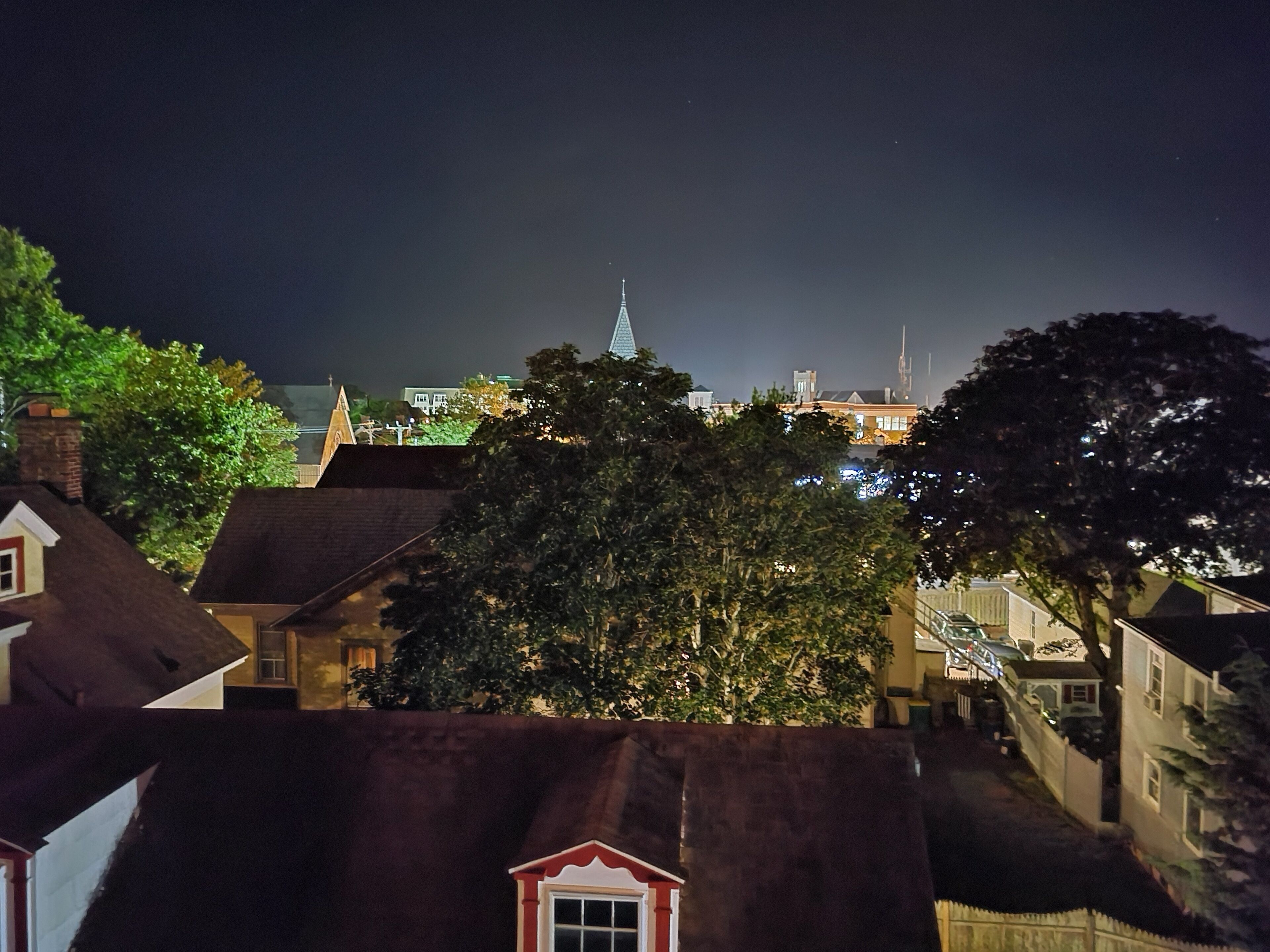 Een nachtzicht van een stad met traditionele architectuur, waaronder een opvallende kerktoren en verschillende woongebouwen.