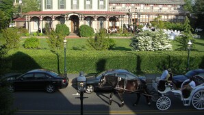 A historic building with a large entrance, a well-maintained garden, and a carriage in the foreground. - Beautiful, Cozy Condo with large private deck! (Cape May)
