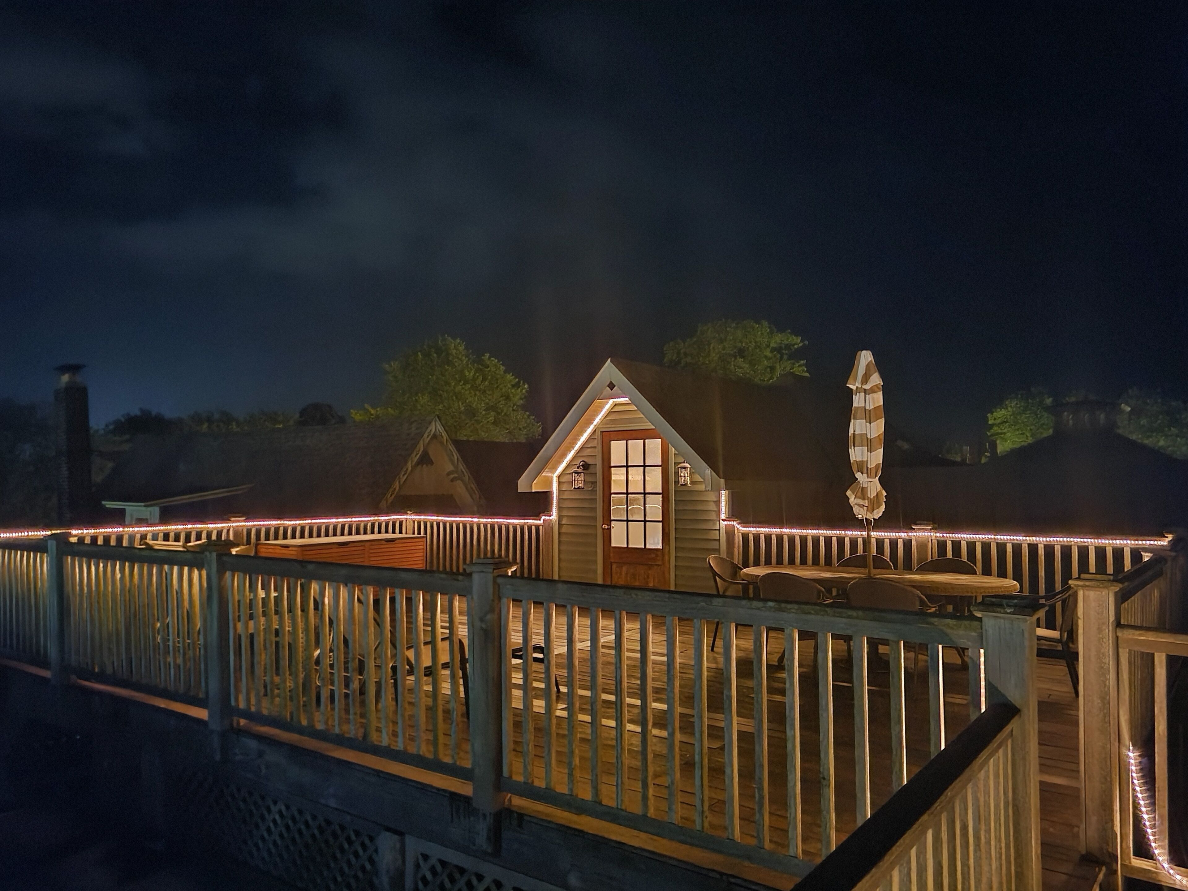 A wooden deck with a railing, a small building with a window, and an umbrella.