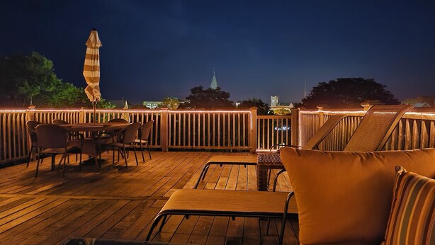 An outdoor deck with wooden furniture and a view of a city skyline at night. - Beautiful, Cozy Condo with large private deck! (Cape May)