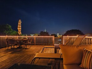 An outdoor deck with wooden furniture and a view of a city skyline at night. - Beautiful, Cozy Condo with large private deck! (Cape May)