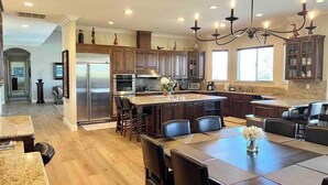 A spacious kitchen with a central island, dark wood cabinets, stainless steel appliances, and a chandelier. - Wine Estate - Private Pickleball, Solar Pool, Golf (Temecula)