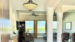 A spacious living room with hardwood flooring, a large chandelier, and a view of the outdoors through large windows. - Wine Estate - Private Pickleball, Solar Pool, Golf (Temecula)