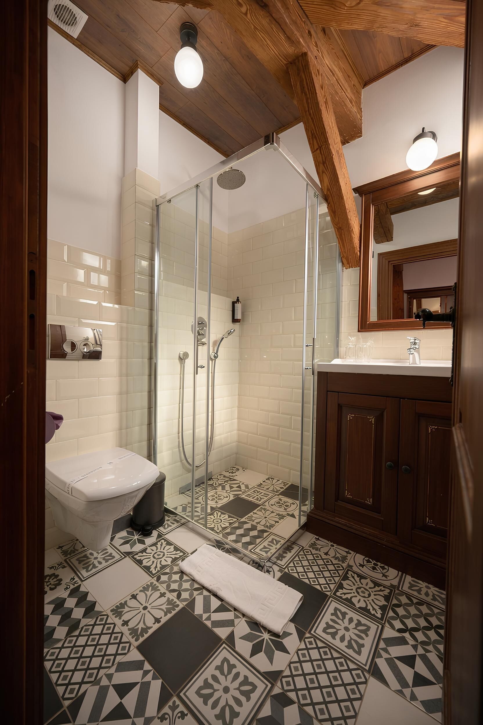A bathroom with a shower, toilet, and sink, featuring patterned tiles and wooden beams.