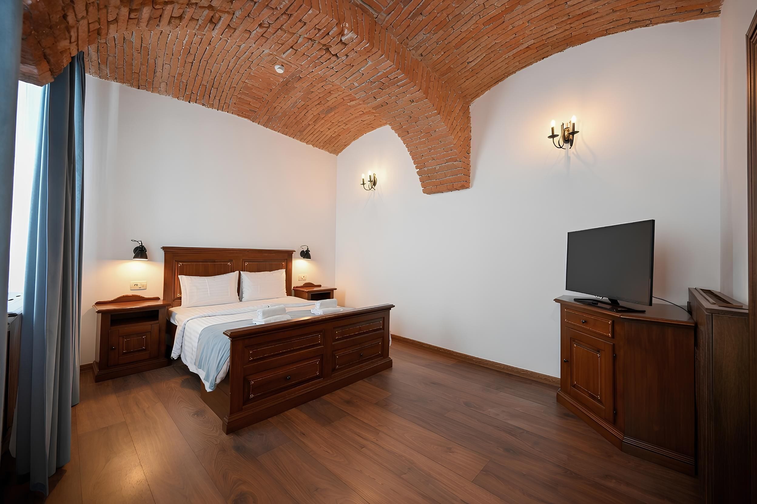 Une chambre avec un plafond en briques, un lit, une télévision, des meubles en bois et un luminaire fixé au mur.