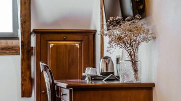 Un bureau en bois, un téléviseur à écran plat, un vase avec des fleurs séchées et une bouilloire posée sur le comptoir.