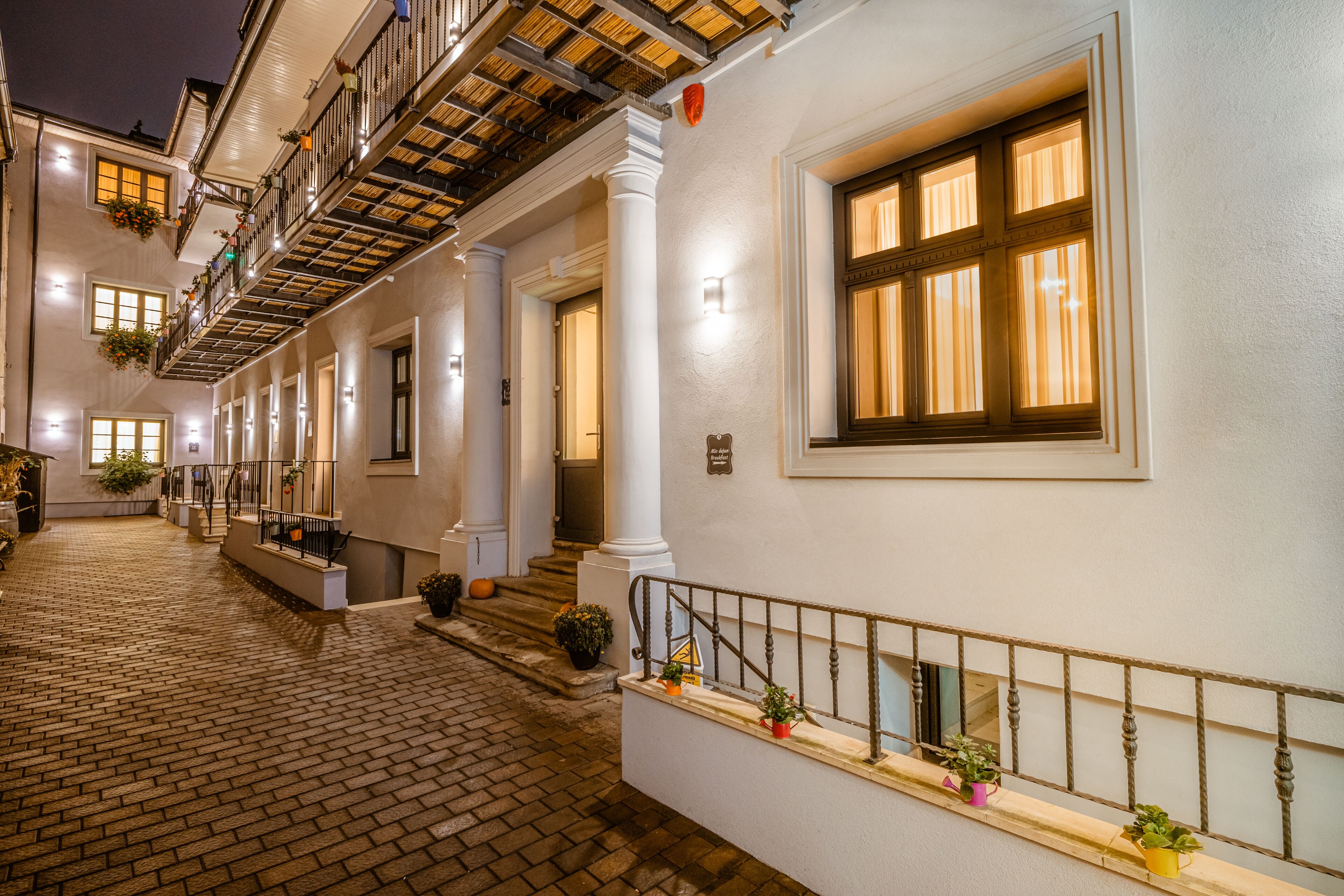 A building with a brick-paved courtyard, white walls, and multiple windows with curtains.