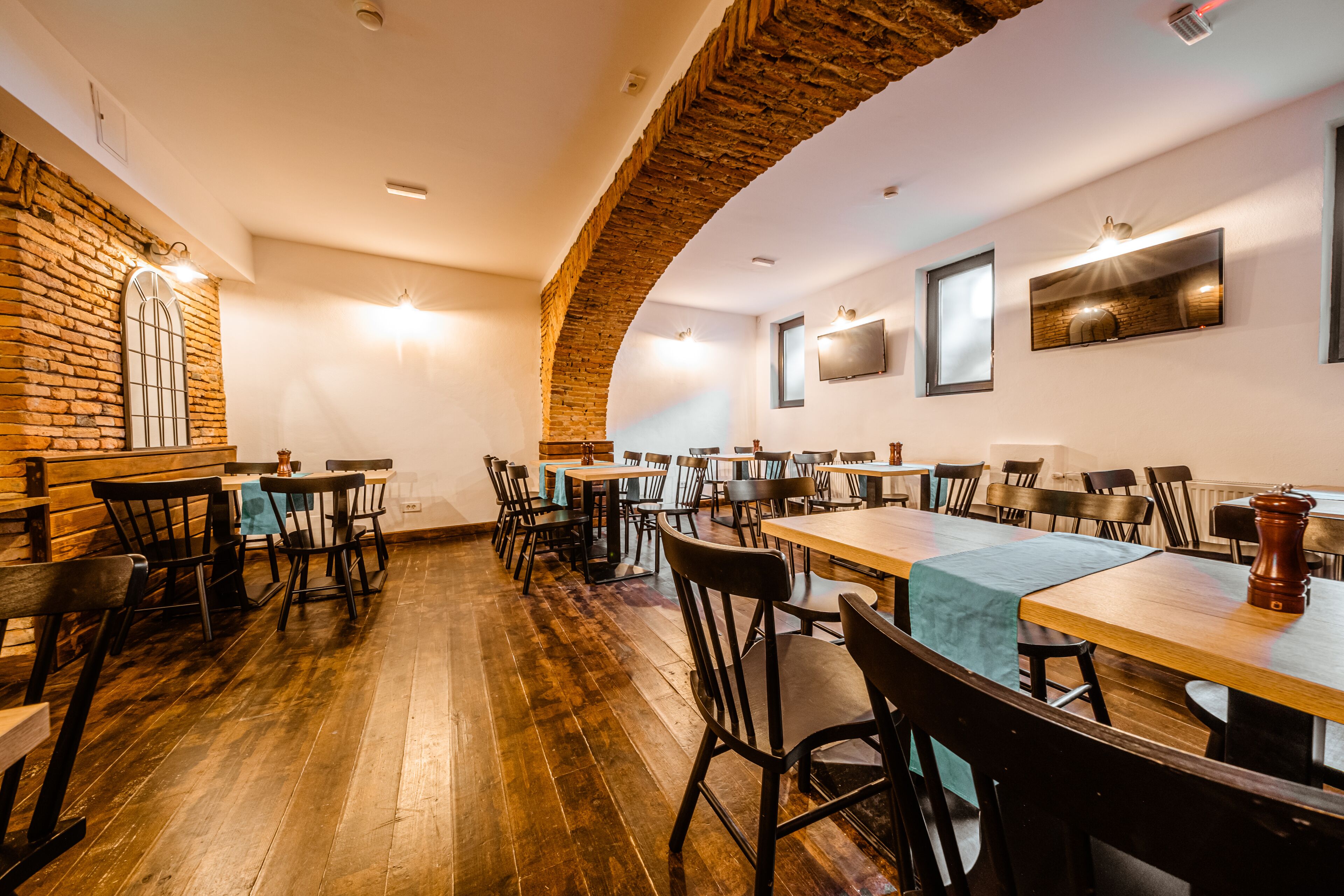 Un restaurant avec des tables et des chaises en bois, des murs en briques et un plafond haut.