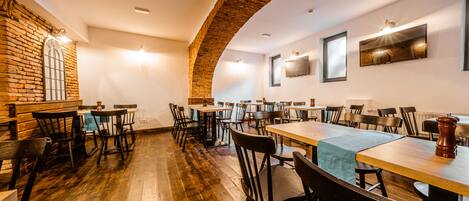 A restaurant with wooden tables and chairs, brick walls, and a high ceiling.