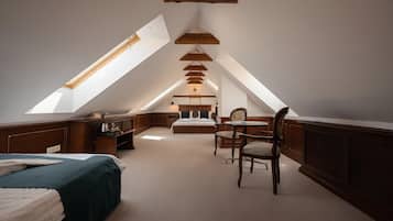 A bedroom with a sloped ceiling, a bed, a chair, a table, and a desk.