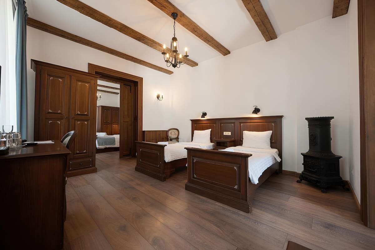 A room with wooden floors, two beds, a desk, a chair, a chandelier, and a fireplace.