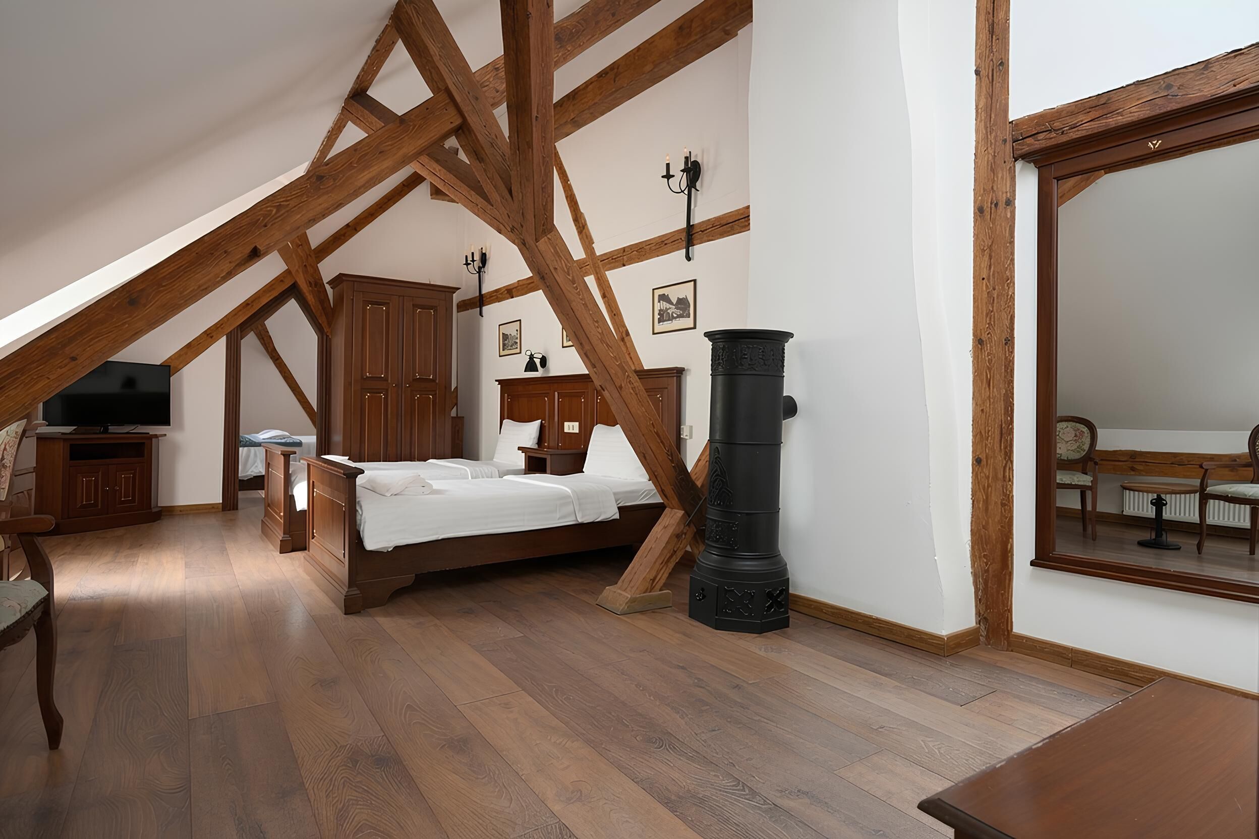 Una camera da letto con soffitto spiovente, travi in legno, un letto, una stufa nera e uno specchio che riflette una sedia e un termosifone.