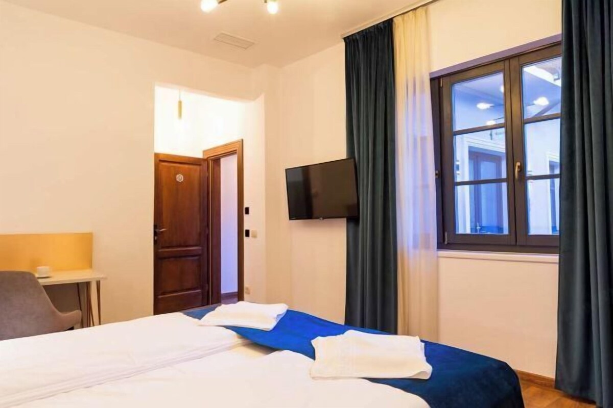 A hotel room with a bed, a desk, a TV, and a window with curtains.