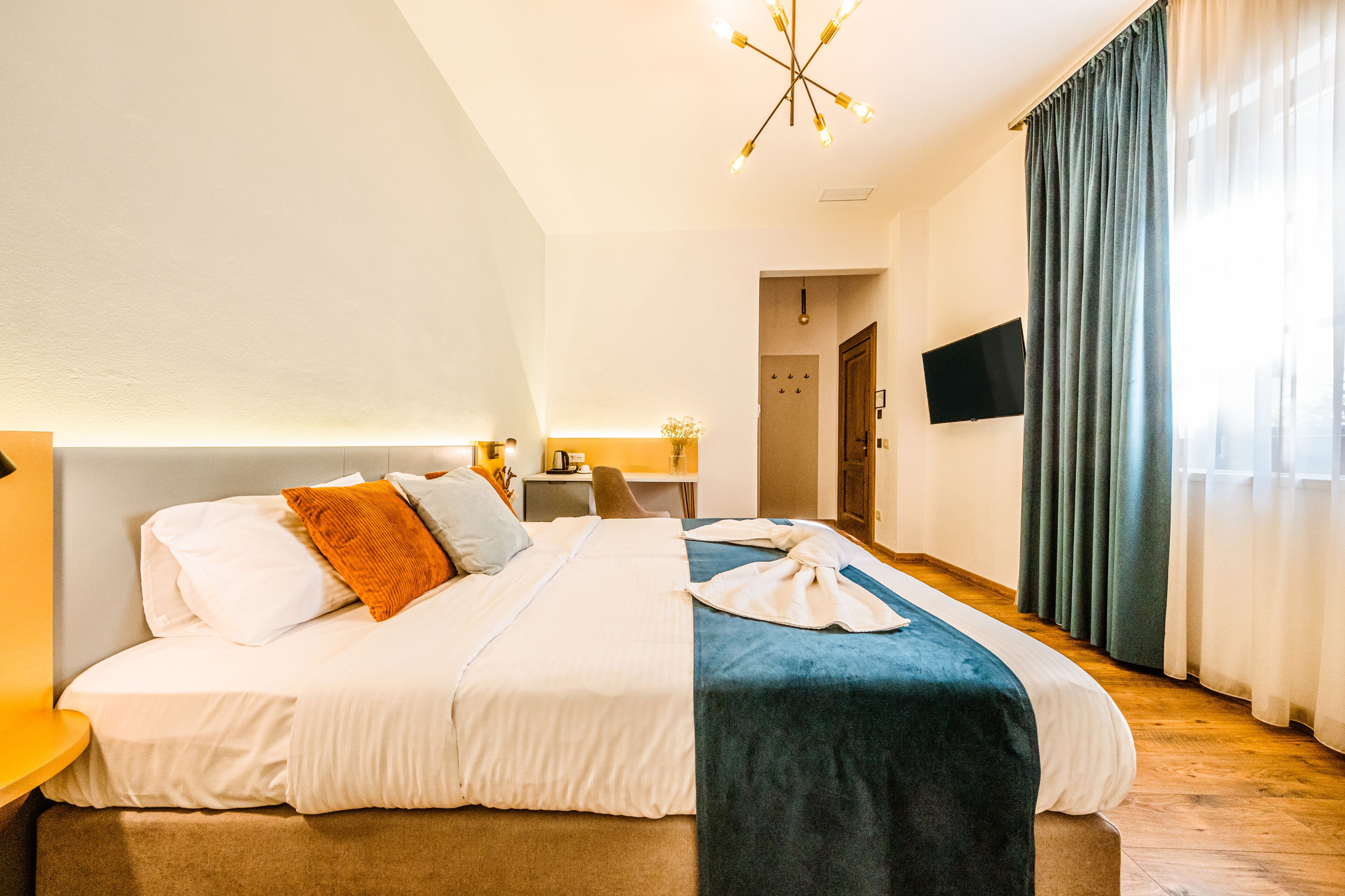 A hotel room with a bed, a desk, a chair, a TV, and a window with curtains.