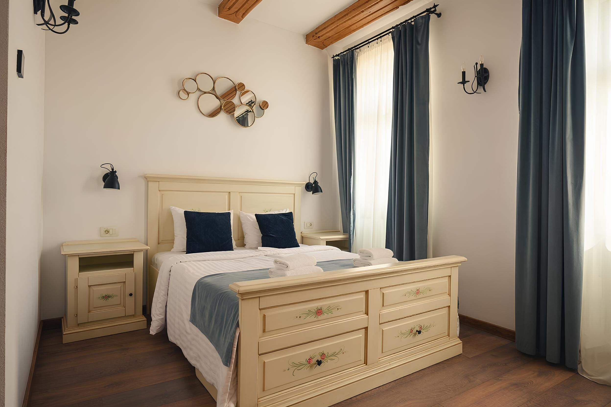 Ein Schlafzimmer mit Bett, Nachttischen, einem Schminktisch, einem an der Wand befestigten Spiegel und einem Fenster mit Vorhängen.