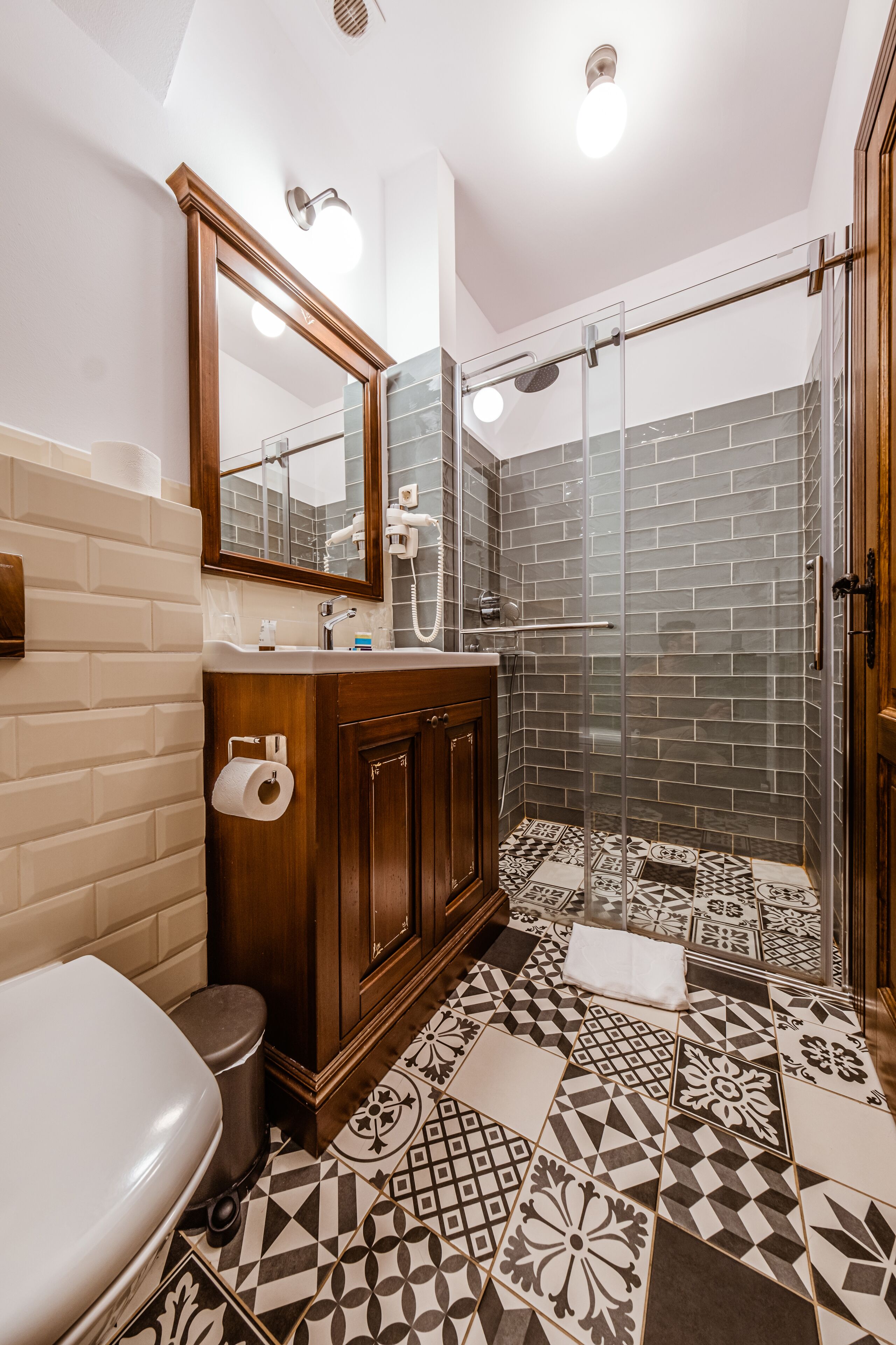 A bathroom with a toilet, a sink, a mirror, a shower, and patterned tiles.