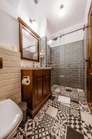 Un baño con inodoro, lavamanos, espejo, ducha y baldosas estampadas.