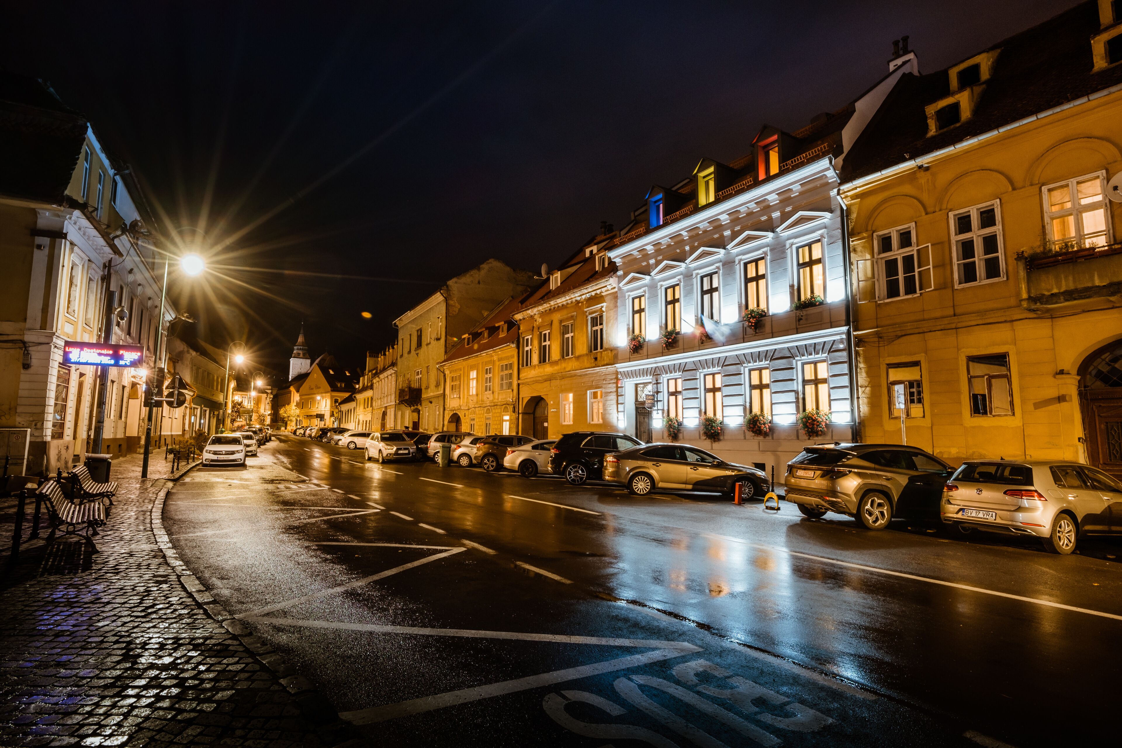 A nighttime street scene with parked cars and historic buildings.