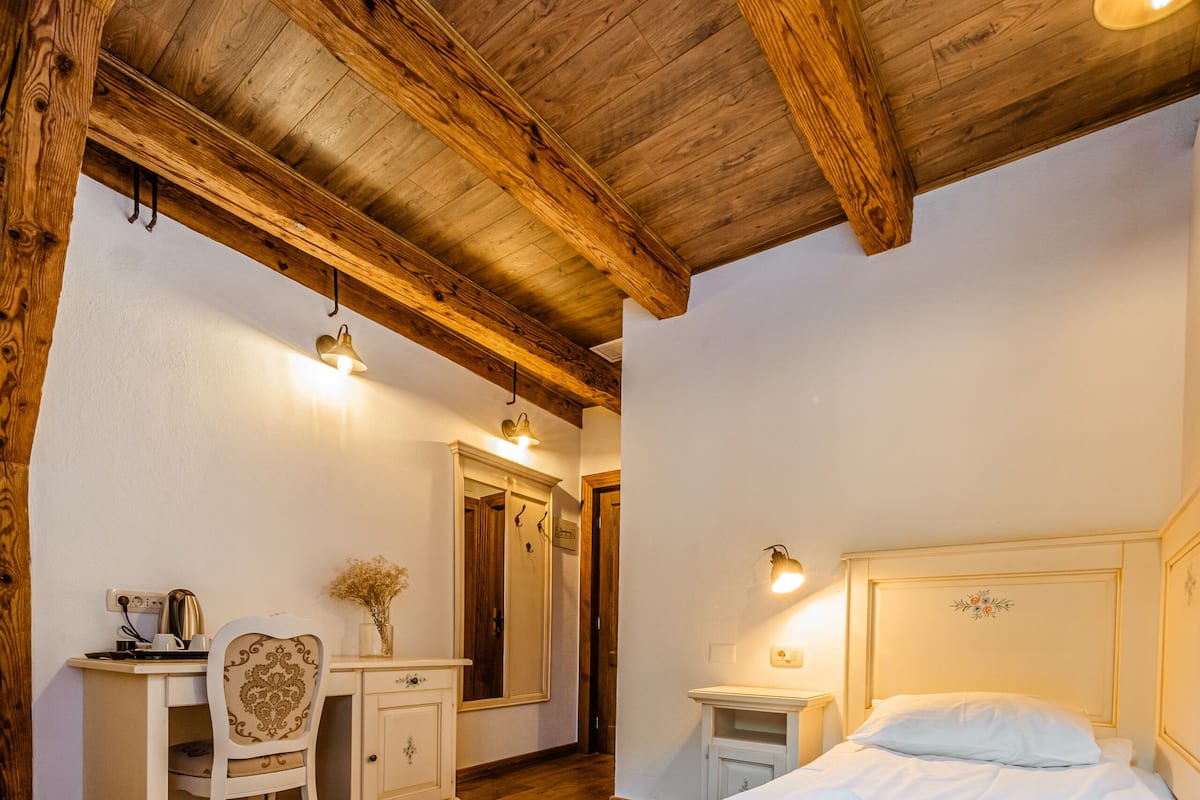 A bedroom with a wooden ceiling, a bed, a desk, and a chair.
