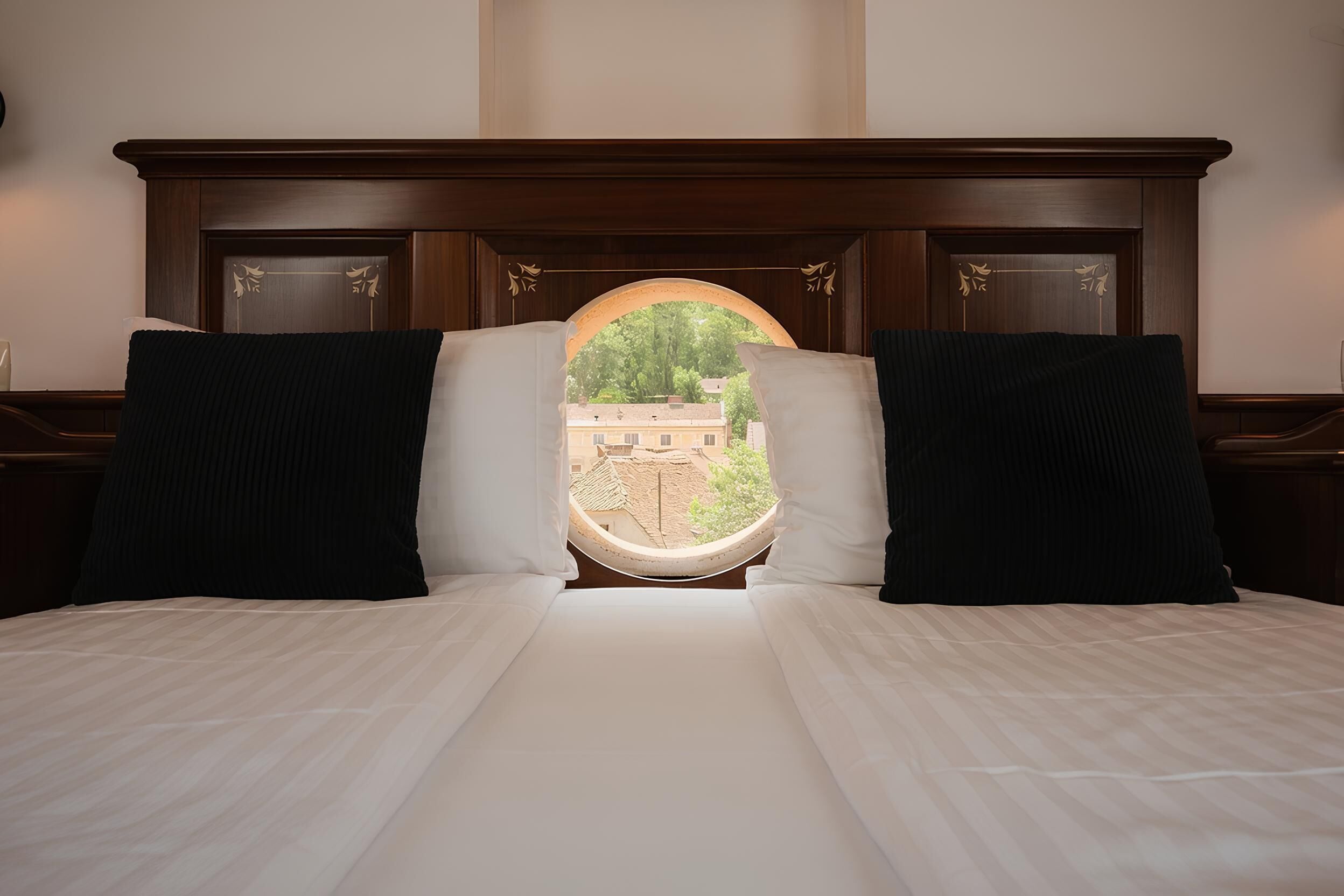 A bed with a view of a building through a window, a wooden headboard, and two pillows.