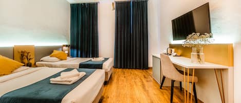 Habitación de hotel con dos camas, un escritorio, una silla, un televisor y suelo de madera.