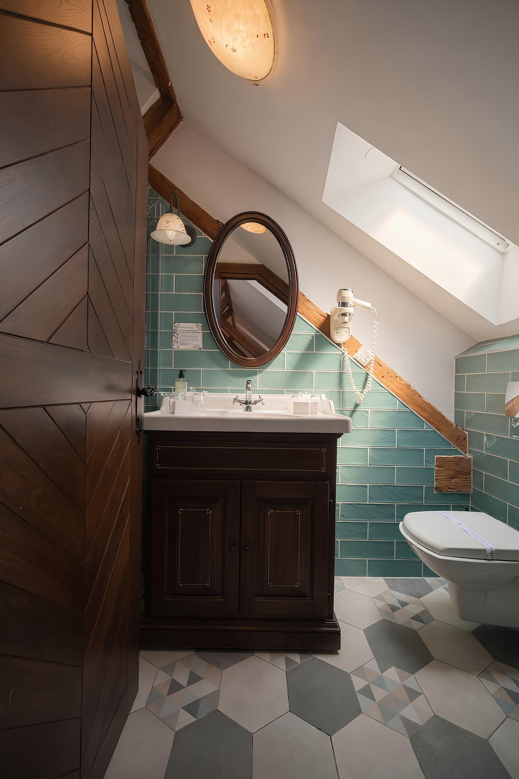 Een badkamer met een houten wastafelmeubel, een ronde spiegel, een wit toilet en een dakraam.