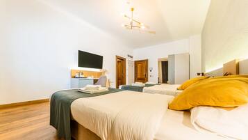 Habitación de hotel con dos camas, un televisor de pantalla plana montado en la pared, un escritorio con una silla y suelo de madera.