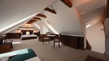 A bedroom with a sloped ceiling, a bed, a desk, a chair, and a small table.
