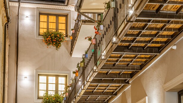 A narrow, well-lit corridor with a wooden staircase and multiple balconies adorned with hanging flower baskets. - Casa Chitic Hotels (Brasov)