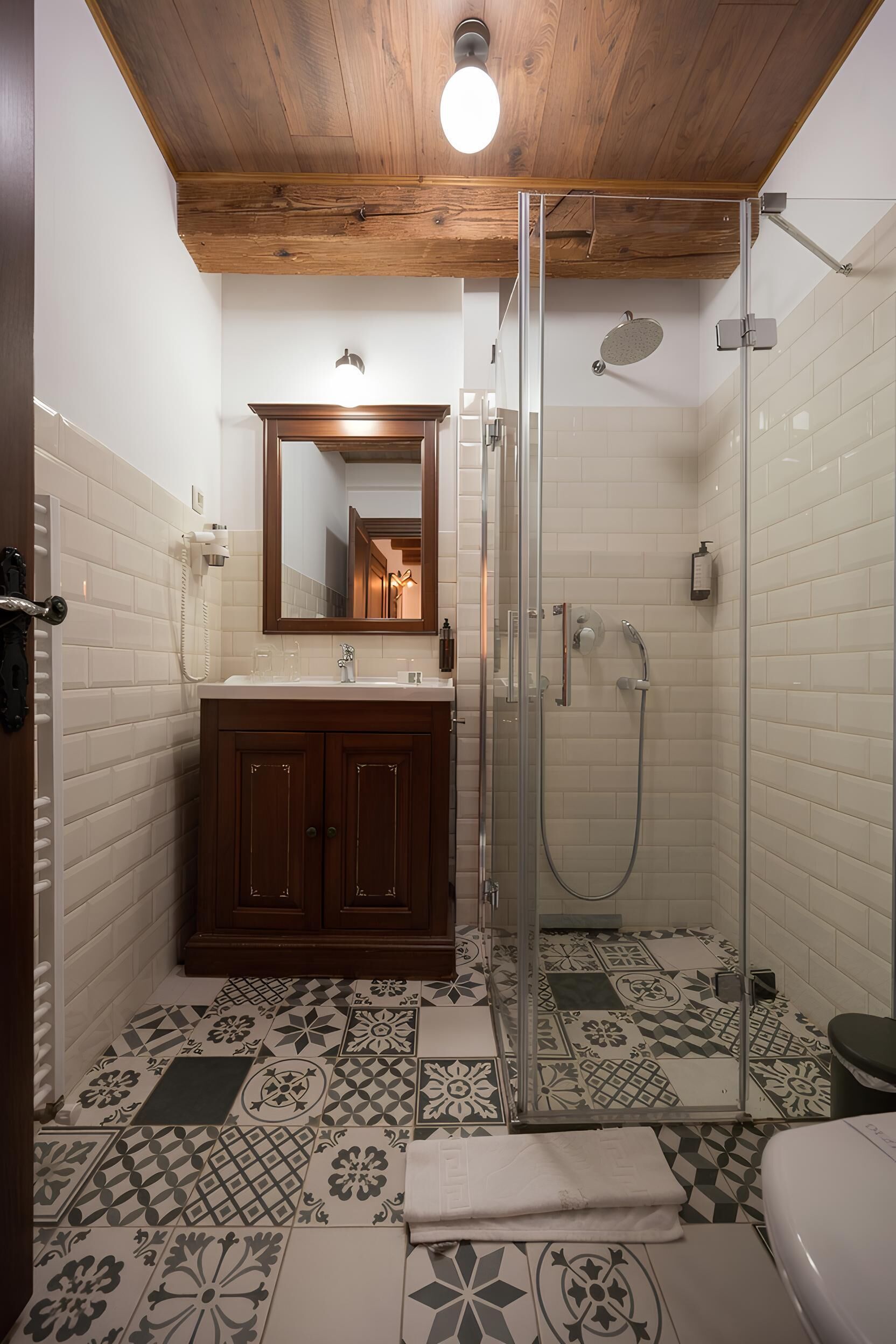 Ein Badezimmer mit Dusche, Toilette und Waschbecken, mit gemusterten Fliesen und Holzbalkendecke.