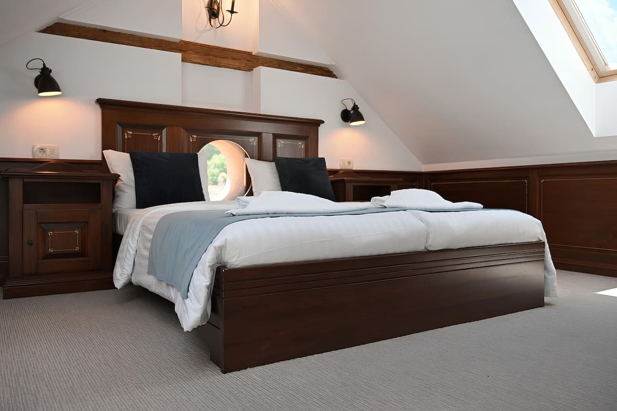 A bedroom with a large bed, wooden headboard, bedside lamps, and a skylight.