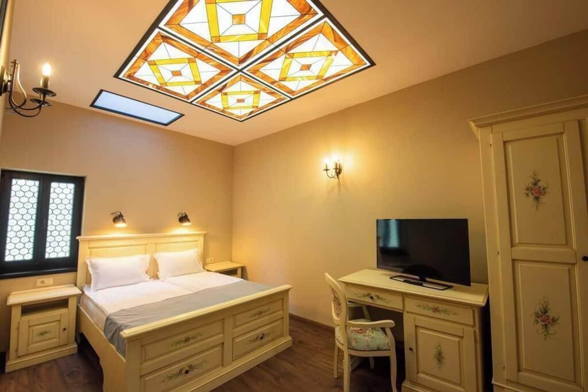 A bedroom with a bed, bedside tables, a desk with a chair, a television, and a wardrobe.