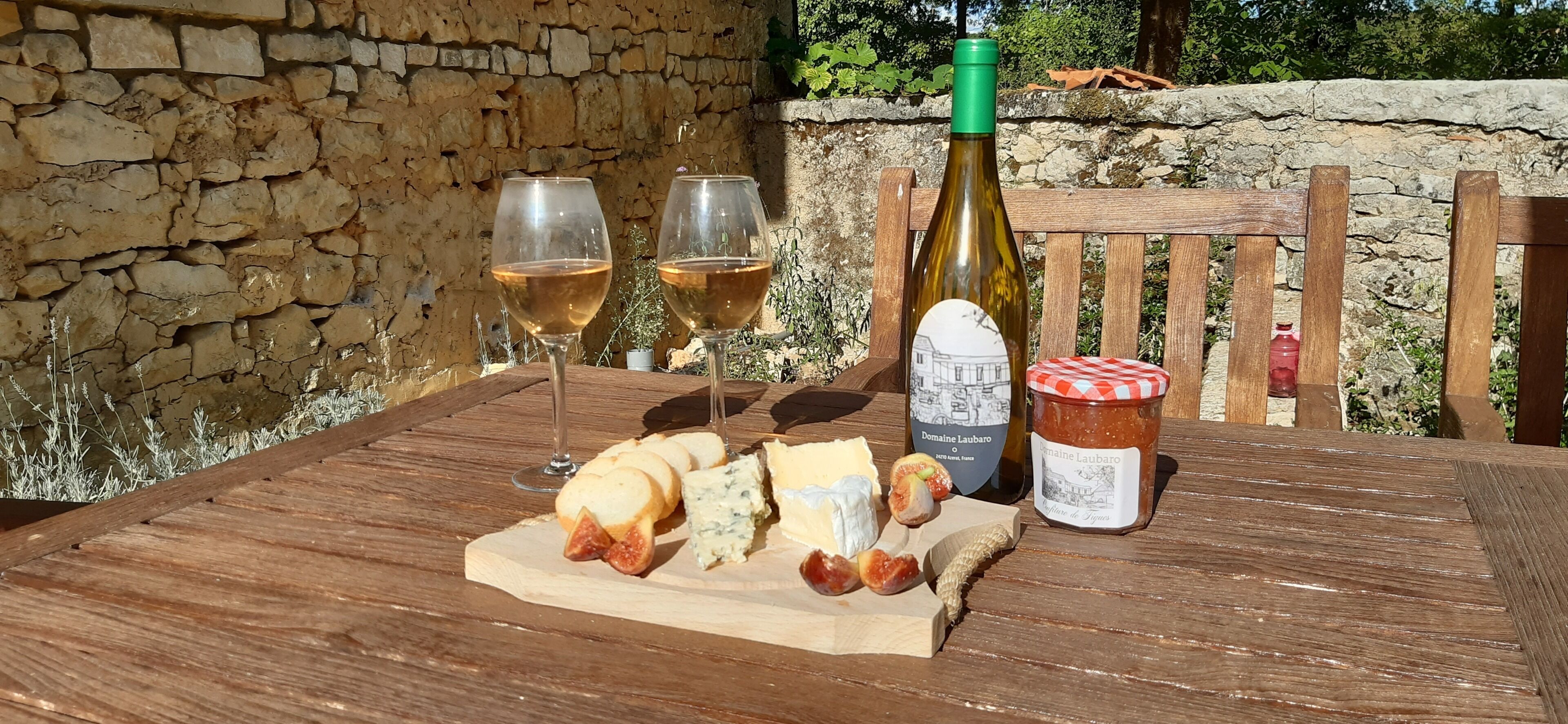 Une table en bois avec une bouteille de vin, deux verres et une variété de fromages et de fruits.