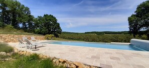 Piscina con sillas de descanso y un muro de piedra.
