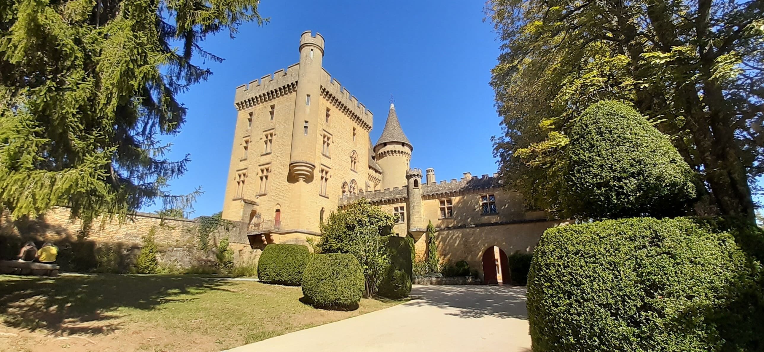 Un château doté d’une tour, entouré de haies bien entretenues et surplombant un ciel dégagé.