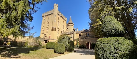 A castle with a tower, surrounded by well-maintained hedges and a clear sky.