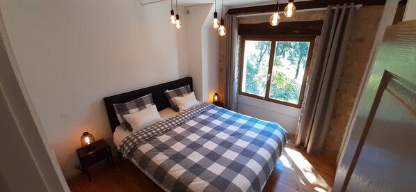 A bedroom with a bed, a nightstand, a window with curtains, and hanging light bulbs.