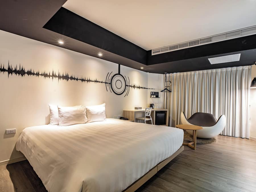 A modern bedroom with a large bed, a desk, a chair, and a unique wall art piece.