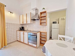 A compact kitchen with a built-in oven, a microwave, and a coffee maker. There is a white refrigerator and a wooden cabinet with shelves.