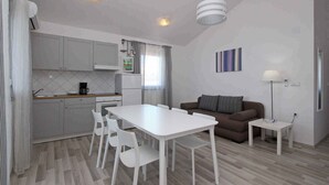 Cozinha moderna com armários brancos, uma mesa de jantar com cadeiras, um sofá marrom e uma pequena mesa lateral com uma luminária.