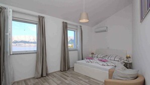 Quarto com cama, cadeira, mesa de cabeceira e janela com cortinas.