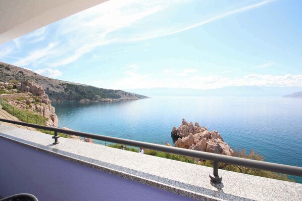 A balcony with a view of a calm sea and rocky coastline.