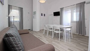 Uma sala de estar moderna com um sofá marrom, uma mesa de jantar com cadeiras, um abajur e uma TV de tela plana na parede.