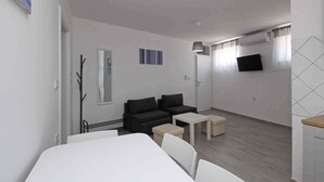 A modern, minimalist room with a large bed, a sofa, a small table, and a TV mounted on the wall. - Holiday apartment with air conditioning and internet, near the sea (Baška)