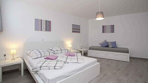 A modern bedroom with a large bed, bedside tables, a bench, and wall art. - Holiday apartment with air conditioning and internet, near the sea (Baška)